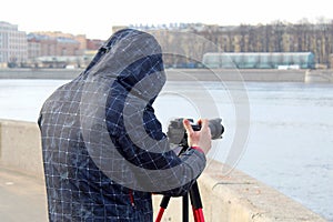 Street photographer in the process of shooting city landscapes. A camera on a tripod. A photographer in a jacket with a hood.