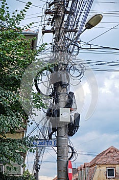 Street pole with TV, internet, telephony, and electricity cables hanging from it in an unorganized matter