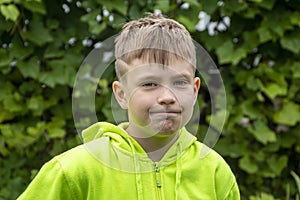Street portrait of a 10-year-old boy with a grimace on his face against the background of nature. Concept: soon to school, summer