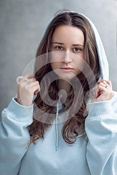 Street portrait of a beautiful young brunette woman in a blue sweatshirt with a hood, lifestyle, no make-up, look at the camera
