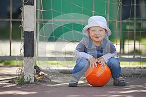 Street portrait of the cute little boy playing with the orange ball