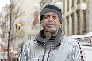 Street portrait of an elderly man 50-55 years old wearing a black hat on a neutral European urban background.