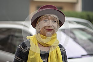 Street portrait of an elderly woman in a fashionable hat and yellow scarf on the background of a European urban landscape, medium