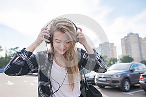 Street portrait of a girl in casual clothing, walking around the city with headphones and listening to music