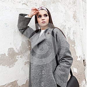 Street portrait glamour woman in fashionable bandana in stylish gray coat with leather black handbag near vintage wall  outdoors.