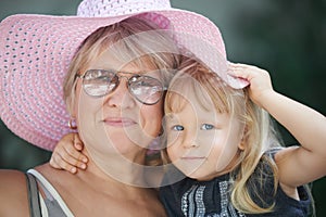 Street portrait of the grandmother with the granddaughter in a pink summer hat