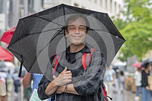 Street portrait of a happy man 50-55 years old with a black umbrella in his hands on a summer city street