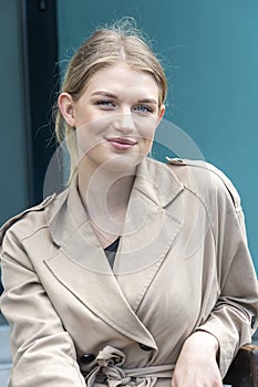 Street portrait of a happy young and beautiful blonde girl 20-25 years old in a light raincoat, sitting on a chair on the street.