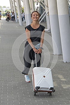 Street portrait of a laughing woman 30-35 years old with a suitcase at the train station, General plan,