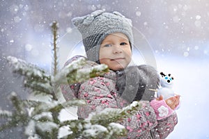 Street portrait of the little girl in the cat hat with a snowman enjoying first snow