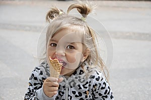 Street portrait of a little girl eating red ice cream in a cone waffle cone. Concept: sweetness for children, summer heat, satisfy