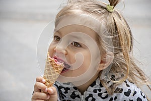 Street portrait of a little girl eating red ice cream in a cone waffle cone. Concept: sweetness for children, summer heat, satisfy