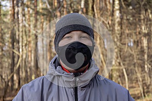 Street portrait of a man of 30-35 years of Eastern appearance in the forest, in a black medical mask, close-up.