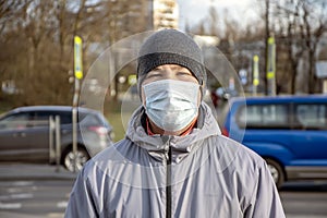 Street portrait of a man of 30-35 years of Eastern appearance in a medical mask, past which people are walking and passing cars