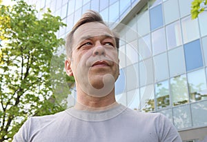 Street portrait of a man 40-50 years old in a gray T-shirt against the background of a business center. Concept: job search after