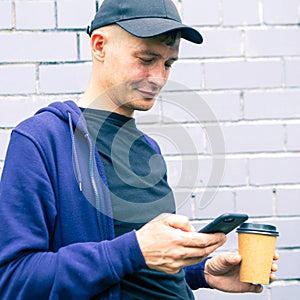 Street portrait of a modern young man with a mobile phone and coffee cup
