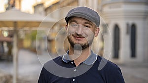 Street portrait of a smiling young man 30 -35 years old in a cap with a beard, looking directly into the camera on a neutral backg