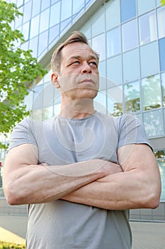 Street portrait of a strong physique man of 40-50 years old in a gray T-shirt against the background of a business center. Concept