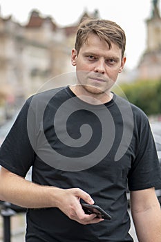Street portrait of a young man 35-40 years old against the backdrop of an urban landscape with a phone in his hands. Perhaps he is
