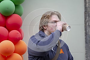 Street portrait of a young man 25-30 years old with blond hair drinking coffee from a paper cup against a background of colorful b