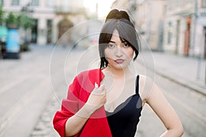 Street portrait of young sexy beautiful Asian woman, wearing stylish fashionable black top and red blazer on one