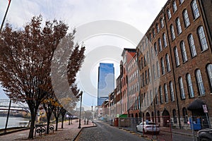 A street on the riverfront with tall red brick buildings and gorgeous autumn colored trees along the street with parked cars