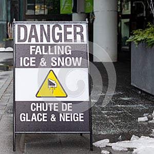 Street sign on the sidewalk warning of the danger of ice and snow falling from the above