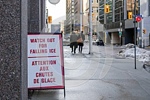 Street sign on the sidewalk warning of the danger of ice and snow falling from the building