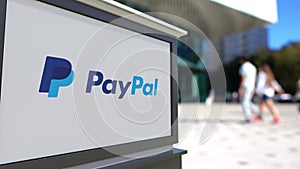 Street signage board with PayPal logo. Blurred office center and walking people background. Editorial 3D rendering