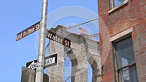 Street signs stand in front of the Brooklyn Bridge around the Fulton Ferry Landing in Brooklyn