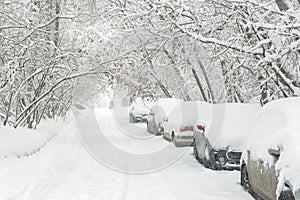 Street during snowfall at winter, Moscow, Russia. Parked cars covered with snow. Scenic view of a snowy city street