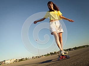 Street Sports: A girl in a bright yellow T-shirt is rolling on a longboard on the city`s asphalt.