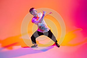 Street style dancer. Young boy dancing hip-hop isolated over gradient yellow pink studio background in neon light
