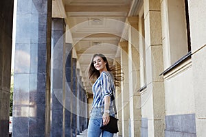 Street Style Outdoors Portrait of Cute Girl. Fashion Woman Smiling. She wearing Print Shirt, Jeans, Bag. Happy Lifestyle