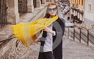 Street style photo of elegant fashionable woman wearing trendy clothes with scarf blowing in wind. Model walking in