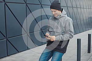 Street style portrait of handsome 30-35 years old man outdoors looking at phone