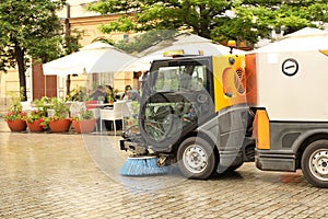 A street sweeper sweeps up a stone pavement with a strong brush in rainy weather. Maintaining clean tourist city. Preventing