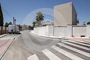 A street in an urbanization with a curved zebra crossing and palm trees