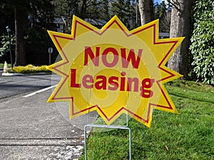 Street view of a bright yellow `Now Leasing` sign outside of a large apatment complex