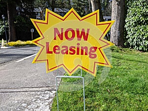 Street view of a bright yellow `Now Leasing` sign outside of a large apatment complex photo