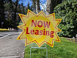 A bright yellow `Now Leasing` sign outside of a large apatment complex photo