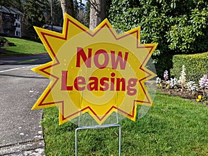 Street view of a bright yellow `Now Leasing` sign outside of a large apatment complex photo