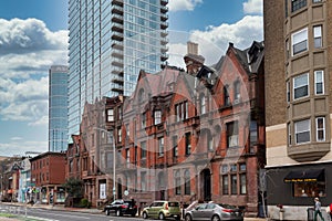 Street view of an old, red brick apartment building with modern office skyscraper behind