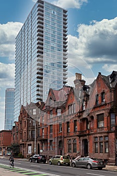 Street view of an old, red brick apartment building with modern office skyscraper behind