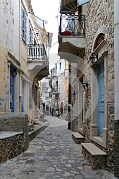 A street view with a stone house with a balcony in the back of the harbour of Calymnos Island