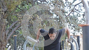 Street workout training. Hispanic man doing parallel bar dips with resistance band on fitness outdoor gym in the park.