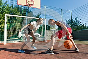 Streetball basketball game with two players, teenagers girl and boy, day on basketball court