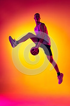 Streetballer. Male basketball player, athlete jumping with ball  on gradient yellow orange background in neon