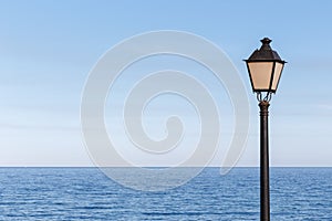 Streetlamp off on a sunny day and the calm sea in the background