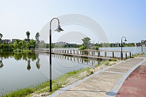 Streetlamps by lakeside path before footbridge in sunny summer m